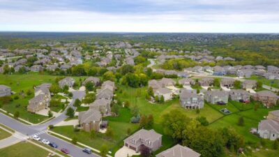 Aerial view of a sprawling suburban luxury community with numerous homes, lush lawns, and winding roads, ideal for building a network in your new luxury community.