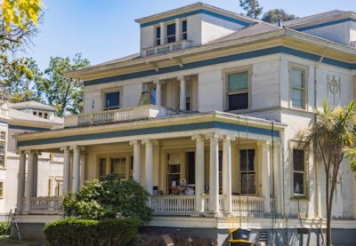 A large historic mansion with tall white columns and a wraparound porch, undergoing exterior updates, representing renovations that drive value in luxury homes